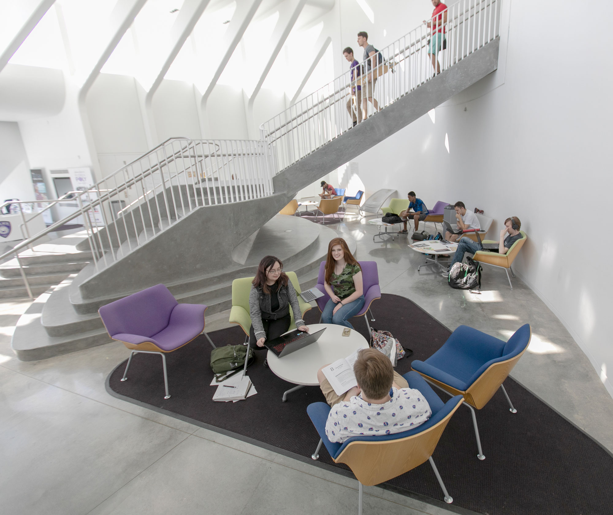 Students sitting in colorful chairs near descending staircase.