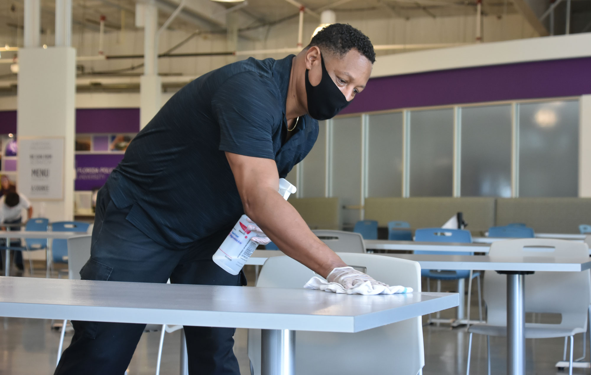Dark skinned male cleaning tables in dining.