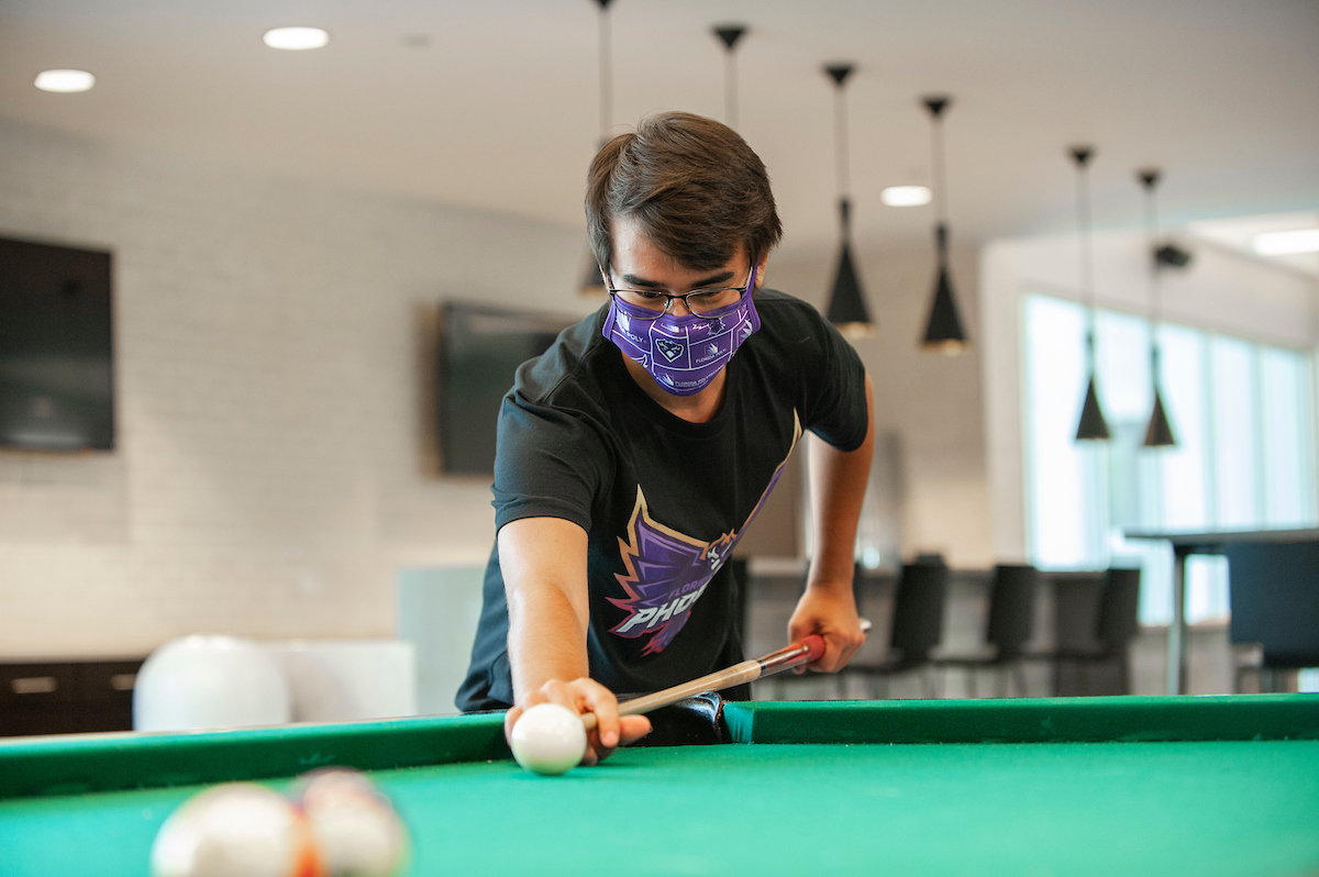 Student playing pool with a mask on.