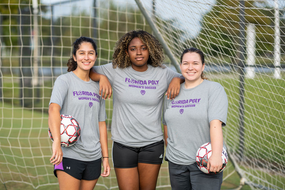 womens' soccer team players in gray shirts stand in front of soccer goal