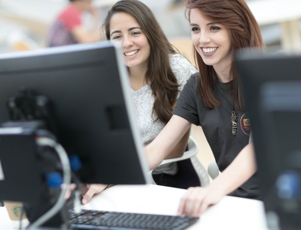 Two light skinned females looking at a computer.