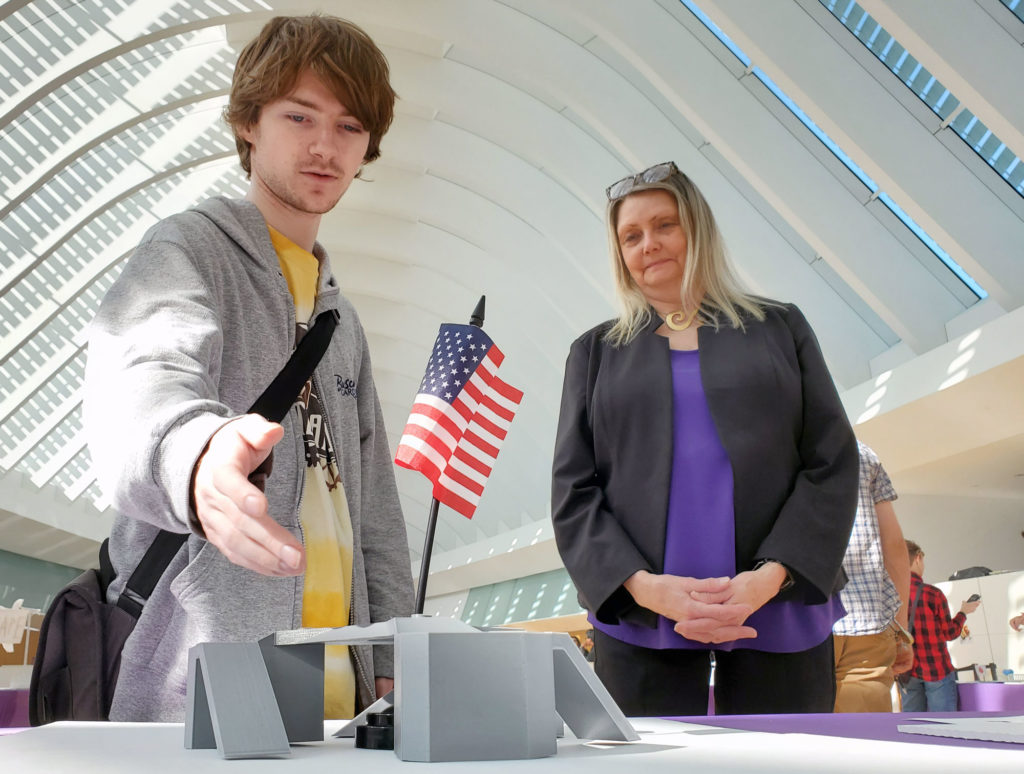 Male student pointing to his art project with teacher.