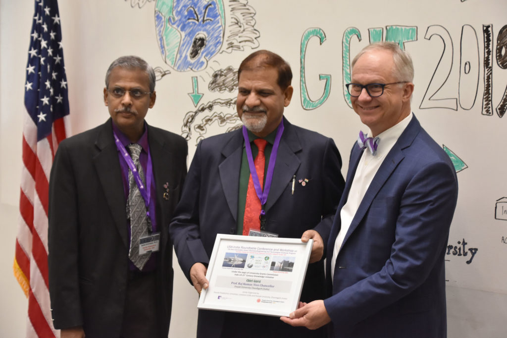 Three men standing in front of room holding a framed award.