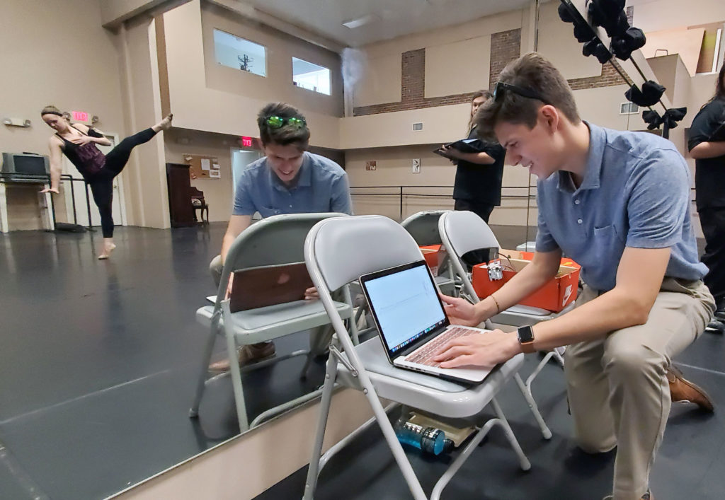 Light skinned male in a dance studio with a computer.