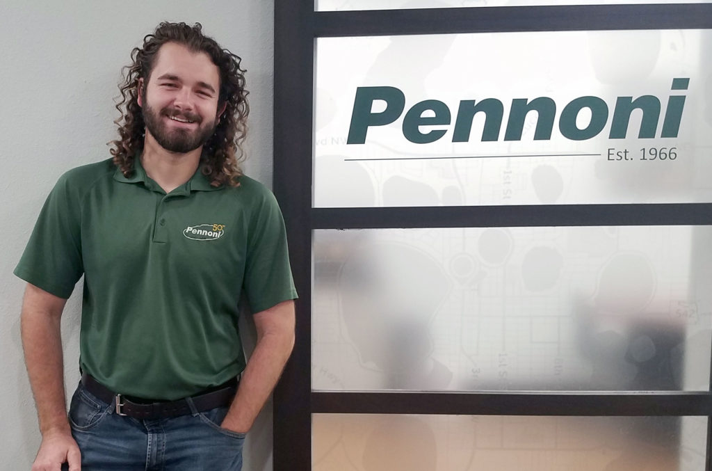 Light skinned male with long hair in front of Pennoni sign.