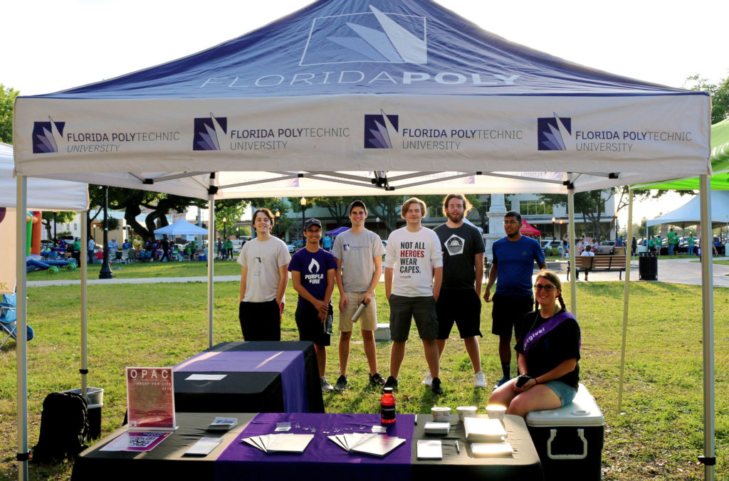 Group of male and female students underneath a Florida Poly tent in a park.