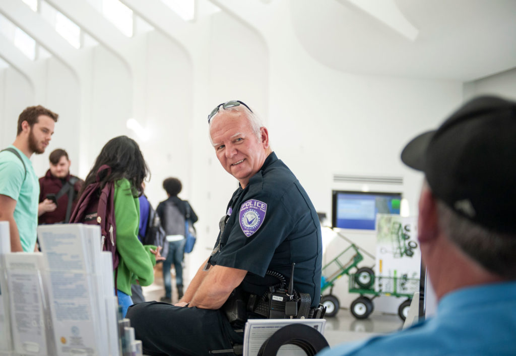 Light skinned male campus office smiling at other officer.