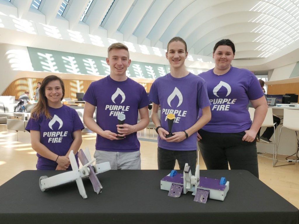 Group of male and females standing in front of a table holding trophies.