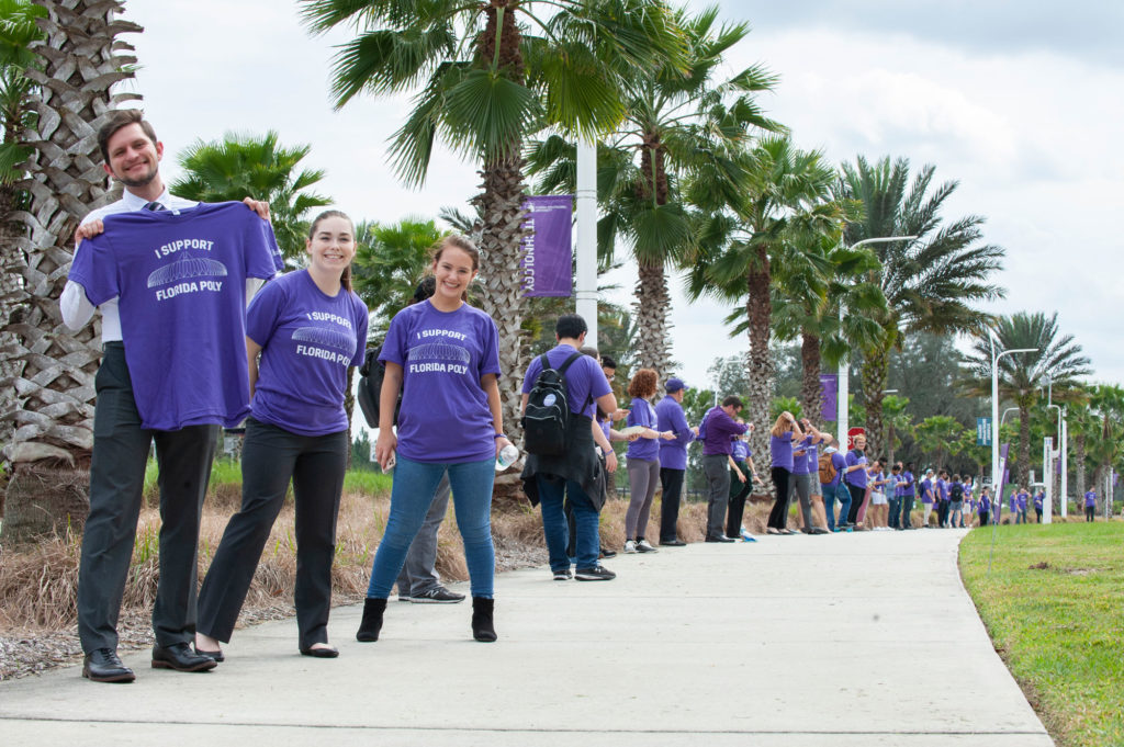 Group of students holding and wearing purple tshirts in a line outside.