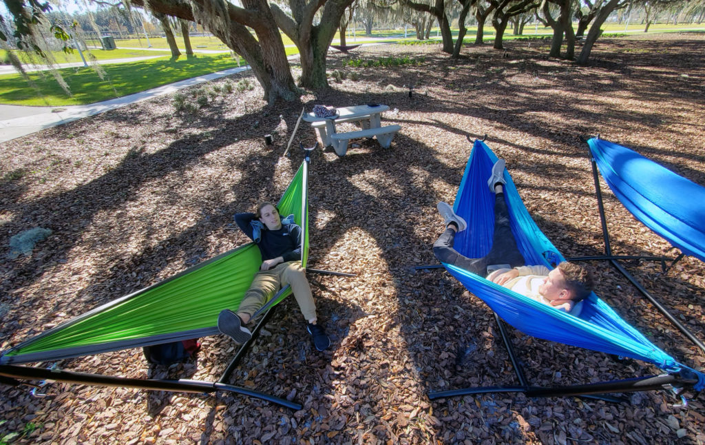 Two light skinned male student laying in two hammocks.